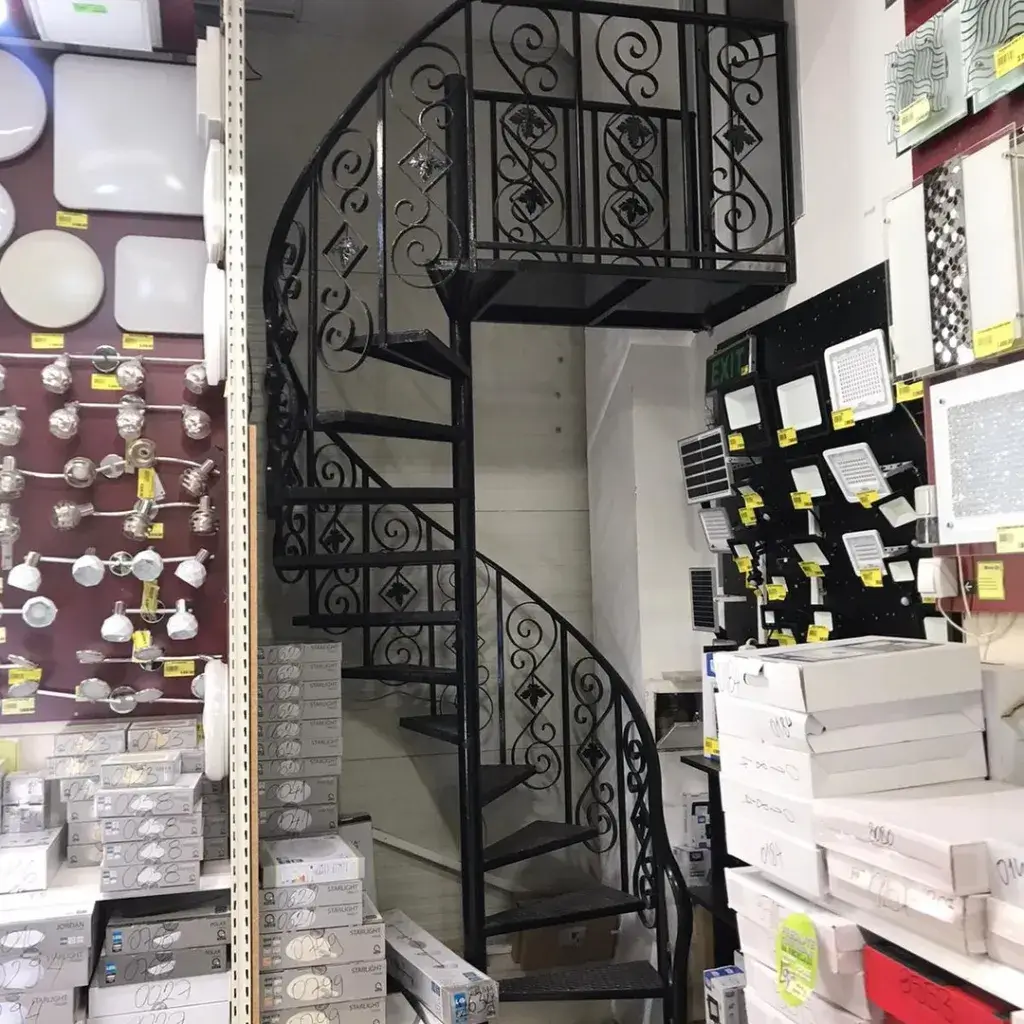 Unutrašnje metalne spiralne stepenice crne boje sa dekorativnom kovanom ogradom.