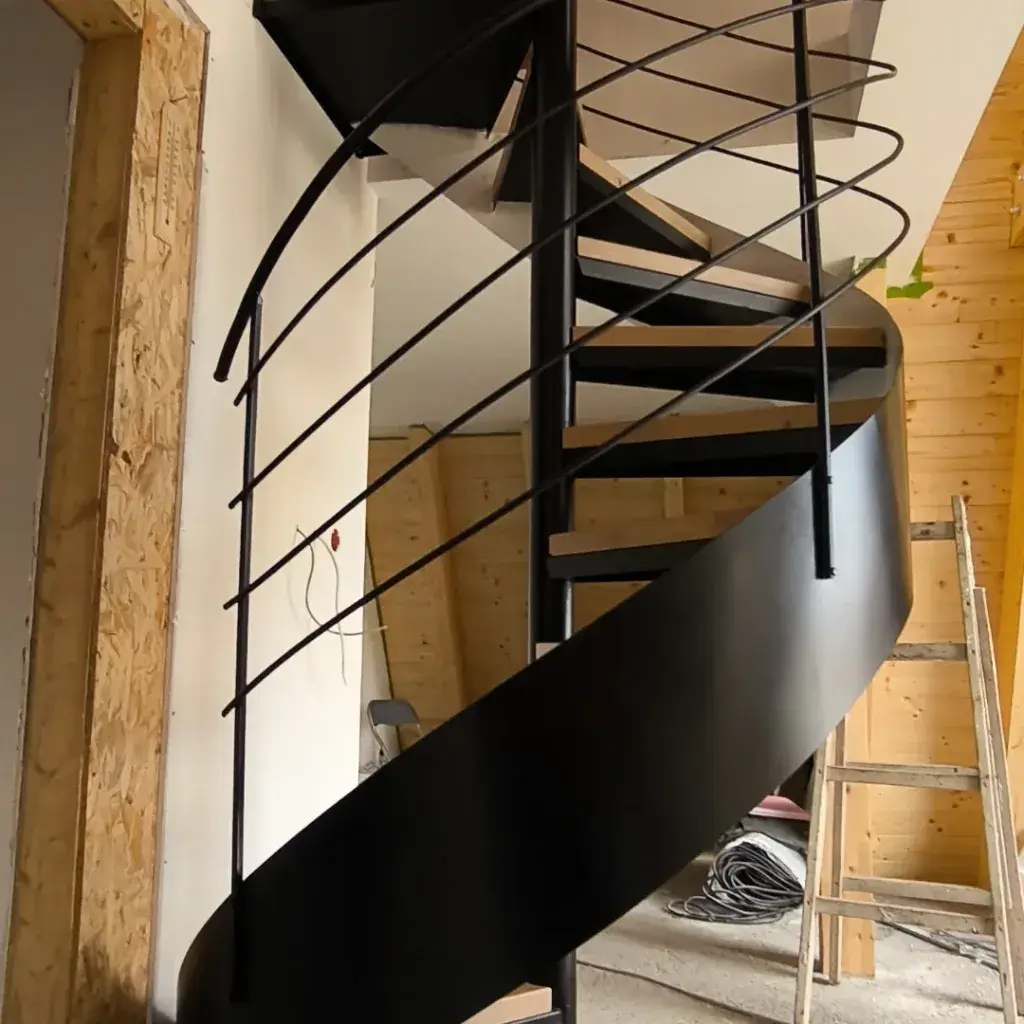 Moderne metal-drvo spiralne stepenice industrijskog dizajna, crni metalni stub nosi celu strukturu, gazištima su od punog svetlog drveta sa, ogradu čine četiri metalne šipke.