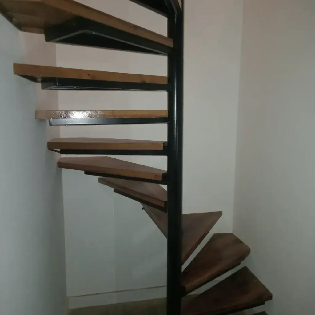 Spiralno unutrašnje stepenište sa metalnom konstrukcijom koju drži metalni stub, gazište je od punog drveta tamne boje.
